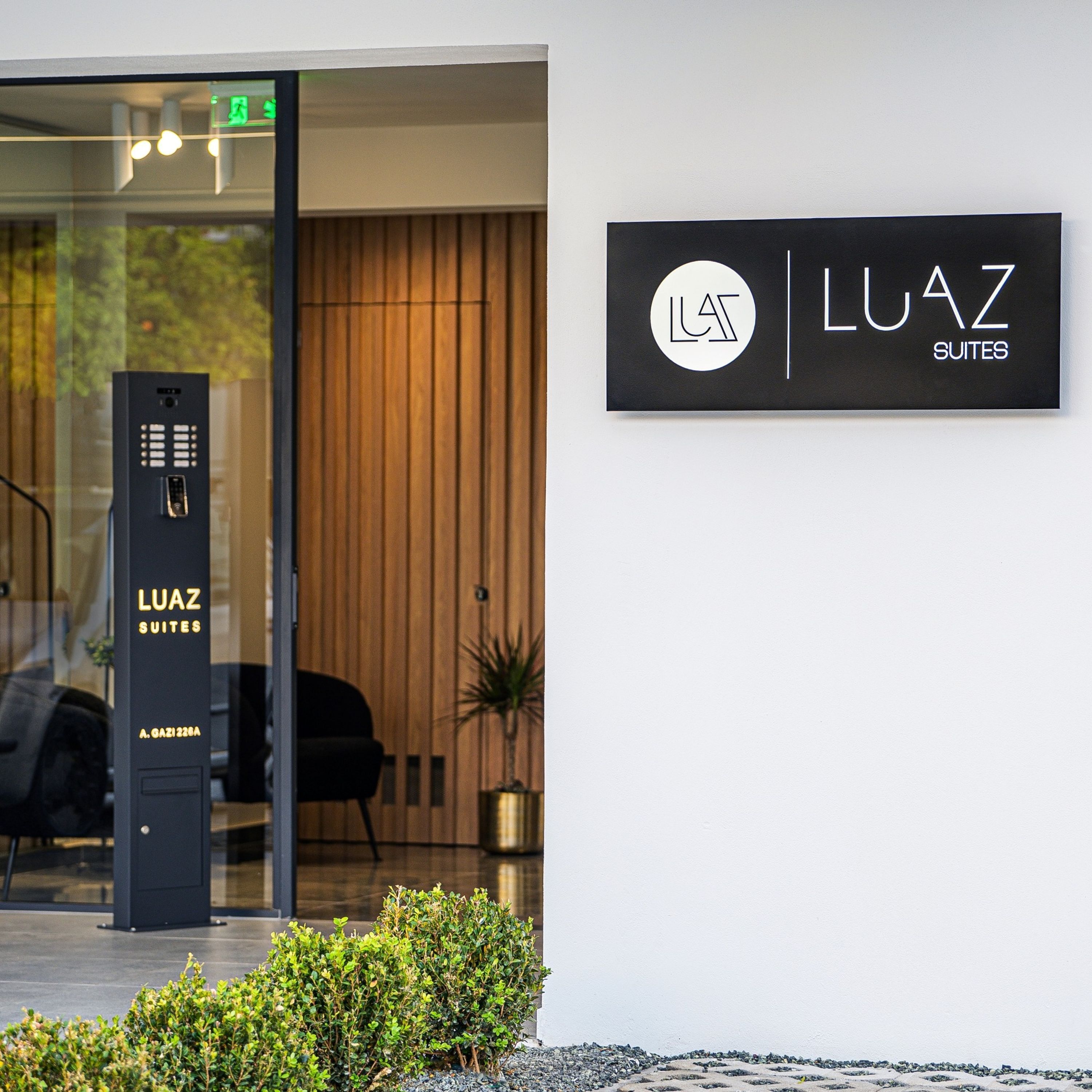 Een moderne gevel met een glazen deur, een keypad buiten en een bord met de tekst 'LUAZ SUITES'.