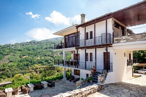 A two-story building with a balcony, stone steps, and outdoor seating. - Paradeisos Flatlet With Garden View (Zagora-Mouresi)