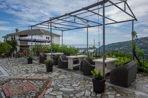 An outdoor patio with stone flooring, wicker furniture, and a pergola structure. - Paradeisos Flatlet With Garden View (Zagora-Mouresi)