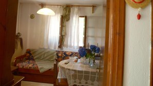 A cozy room with a bed, a dining table with a vase of flowers, and a hanging hat. - Paradeisos Studio With Garden View (Zagora-Mouresi)