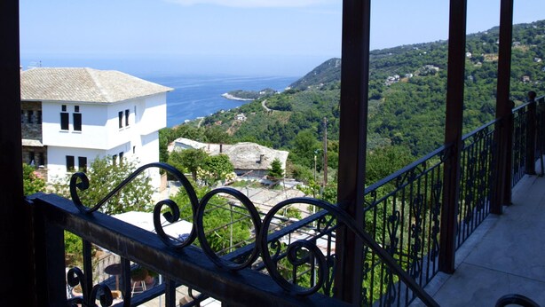 A balcony with a view of a coastal landscape, including a white building and a hill with greenery. - Paradeisos Studio With Garden View (Zagora-Mouresi)