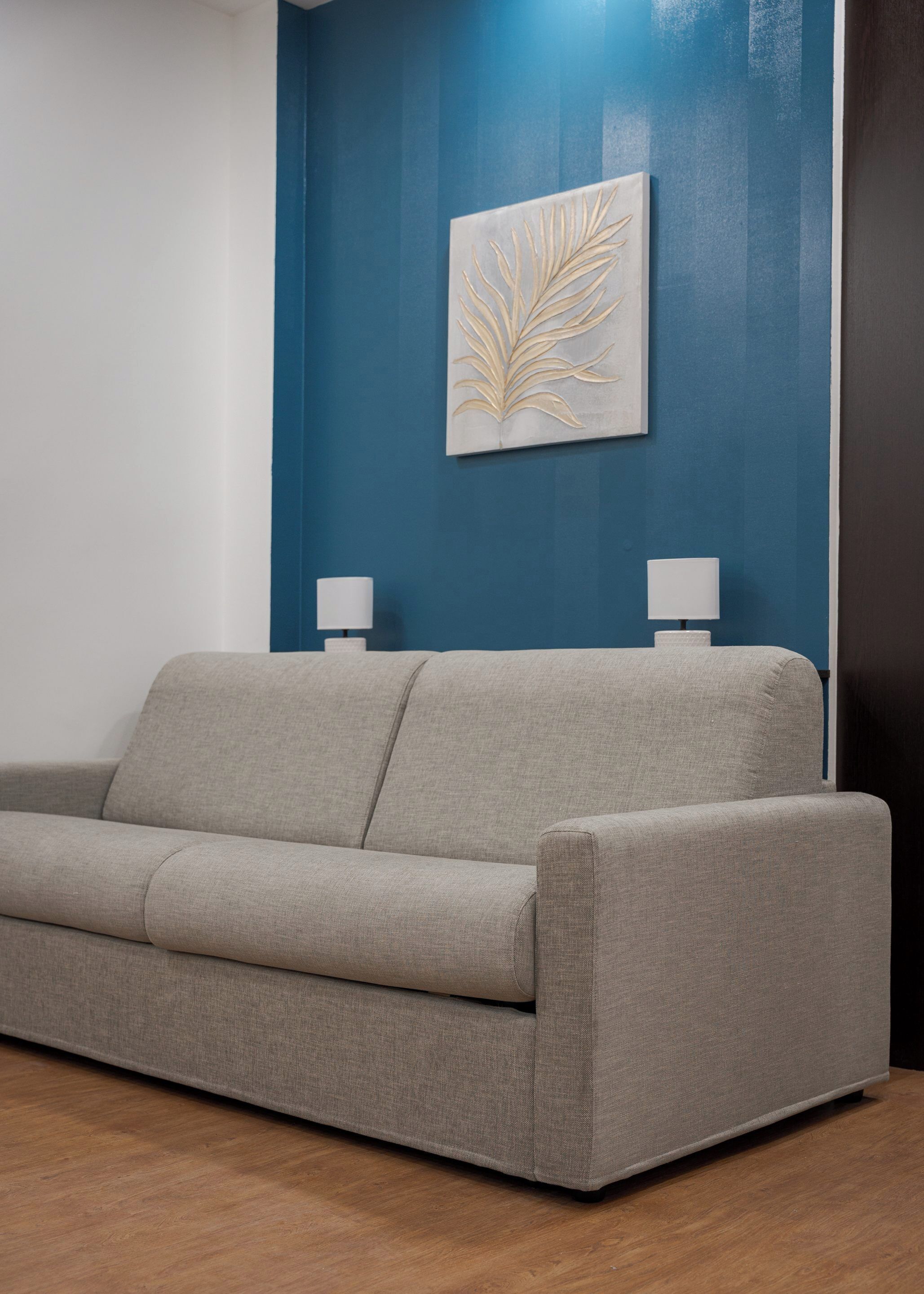 A grey sofa in a room with a blue accent wall and a leaf-patterned artwork.