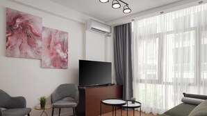 A modern living room with a flat-screen TV, two grey armchairs, a small round table with a plant, and a sofa. - Syntagma Mitropoleos Residence (Athens)