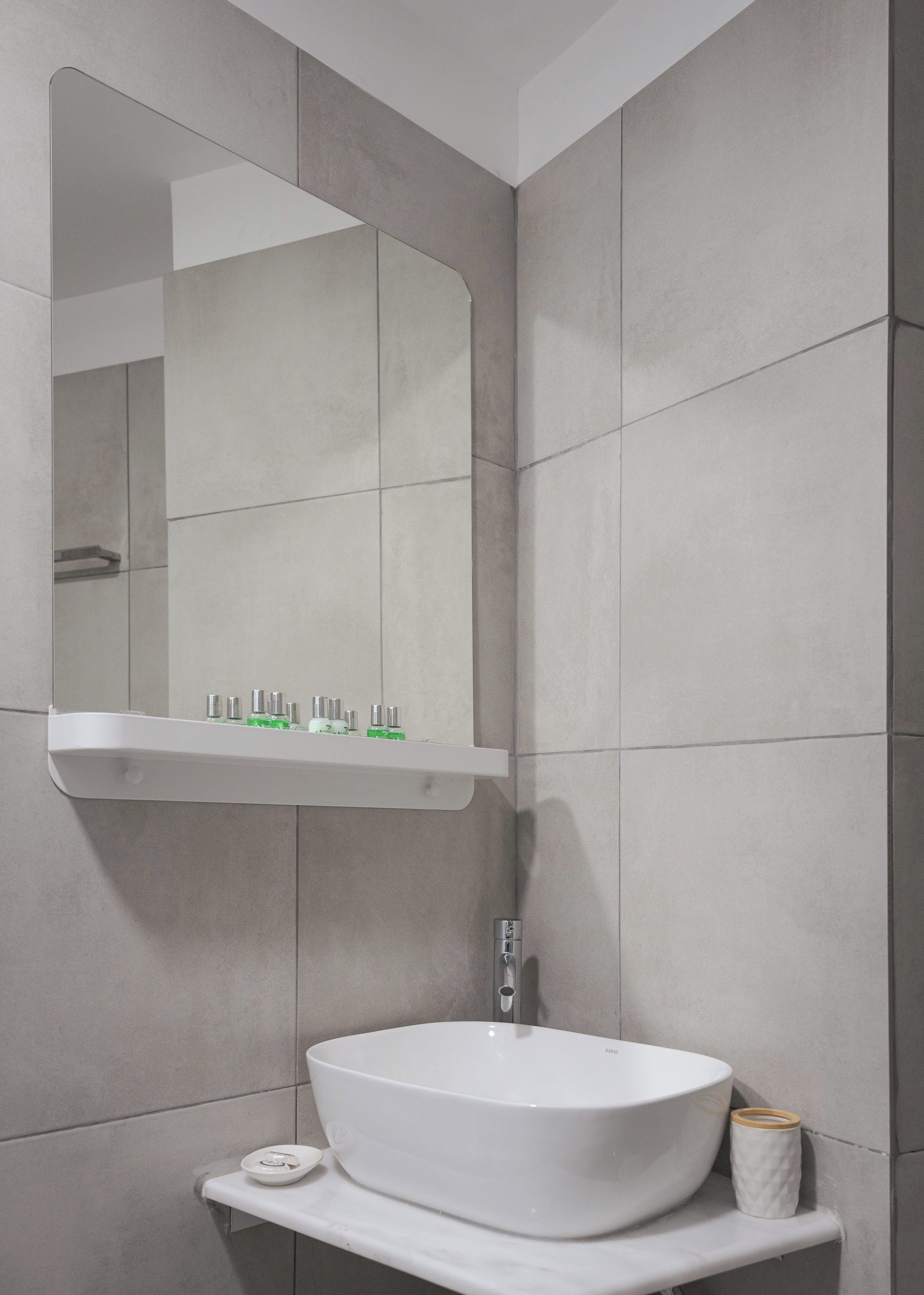 A bathroom with a white vessel sink, a mirror above it, and a shelf with toiletries.