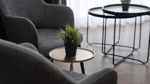 A modern living room with a grey armchair, a small round table with a plant, and a black metal side table. - Syntagma Mitropoleos Residence (Athens)