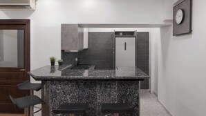 A modern kitchen with a granite countertop, black bar stools, and a built-in oven. - Syntagma Mitropoleos Residence (Athens)