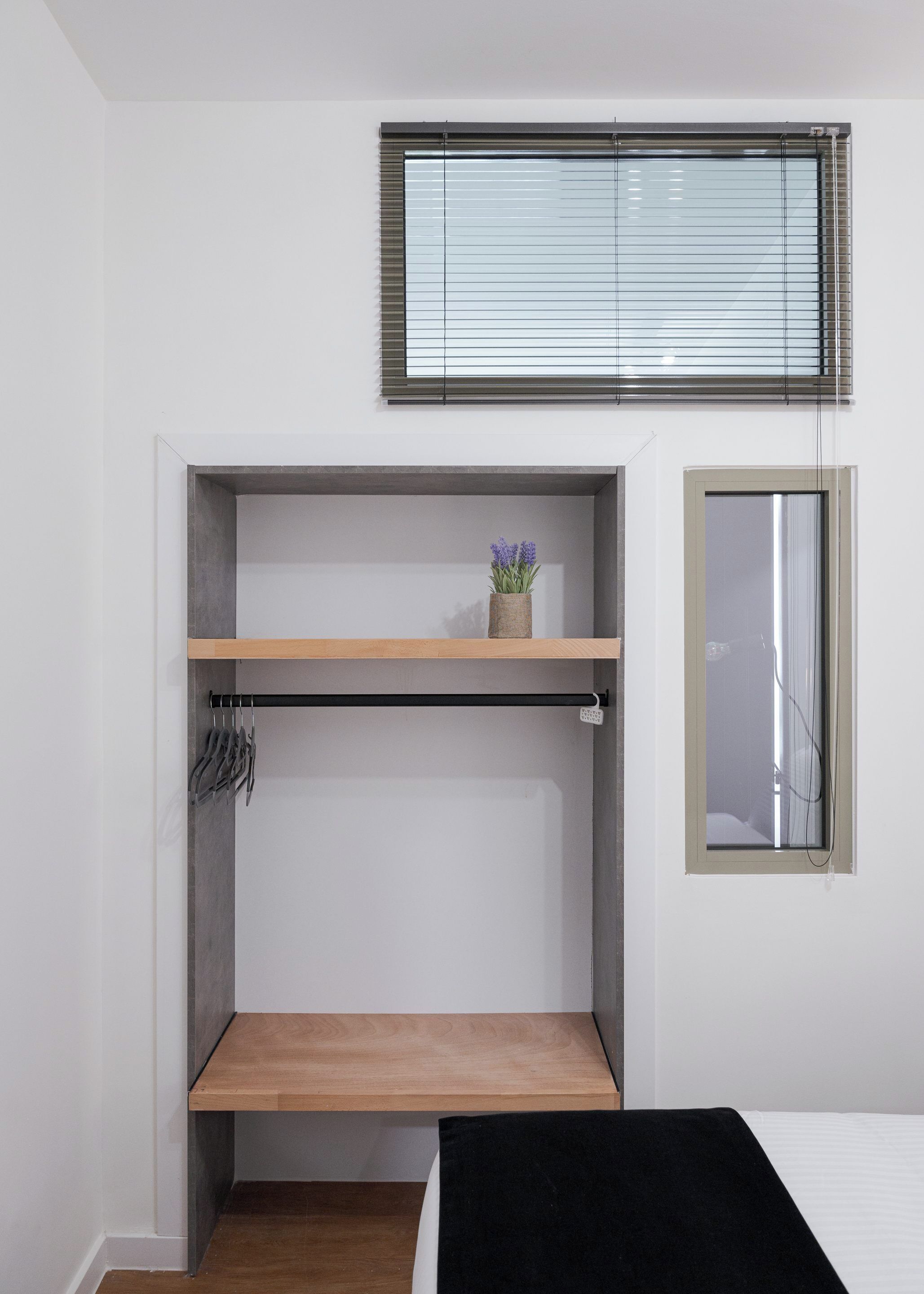 A compact room with a bunk bed, a small shelf with a vase, and a window with blinds.
