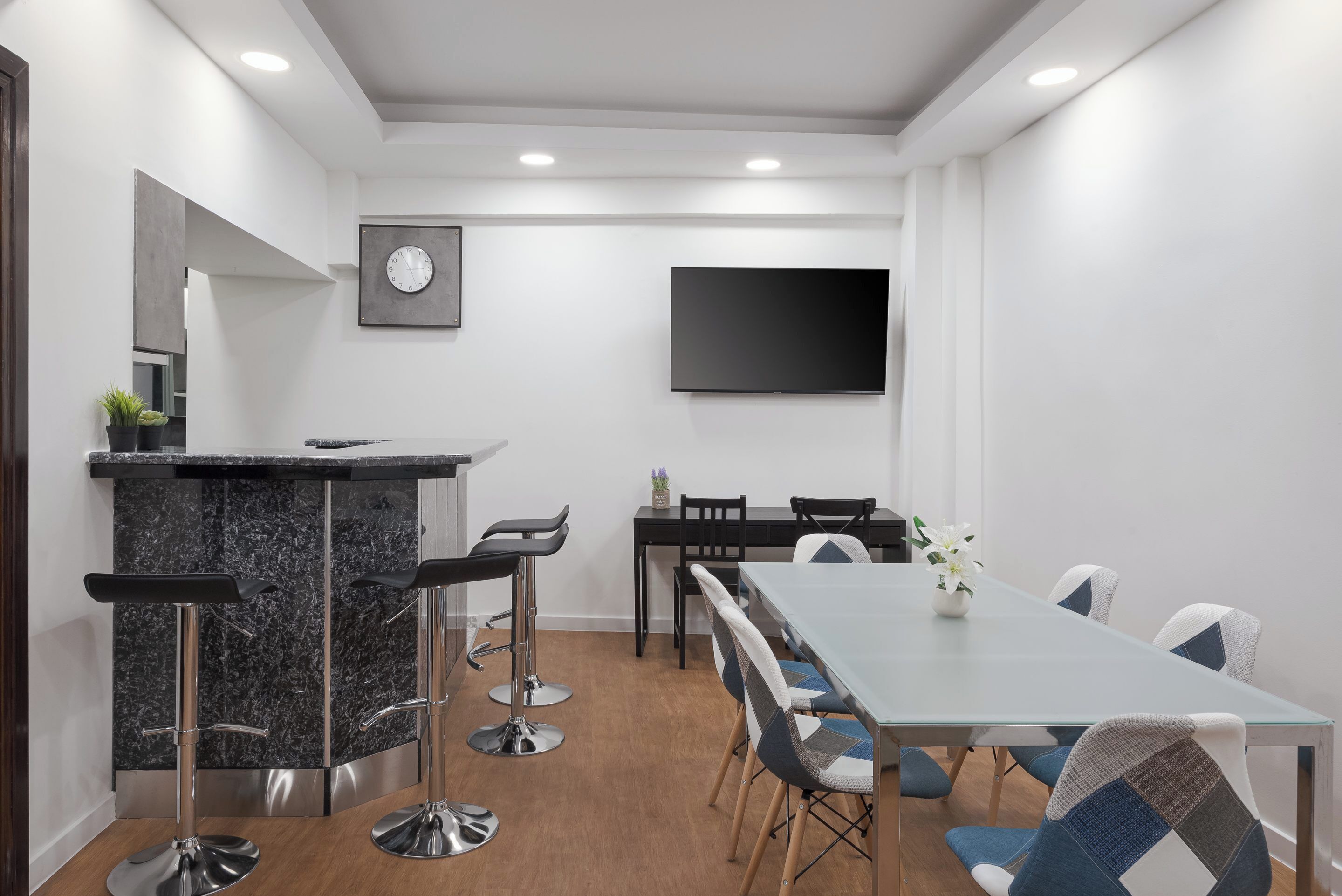 A modern meeting room with a long table, bar stools, and a flat-screen TV on the wall.