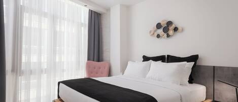 A modern bedroom with a large bed, a wooden headboard, a pink chair, and a wall-mounted decorative piece.
