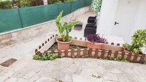 Un jardín con plantas en macetas, valla de madera y mobiliario exterior.