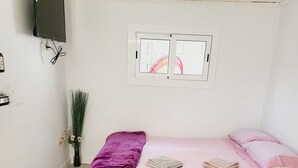 Un dormitorio con cama, ventana, televisor de pared y una planta pequeña.