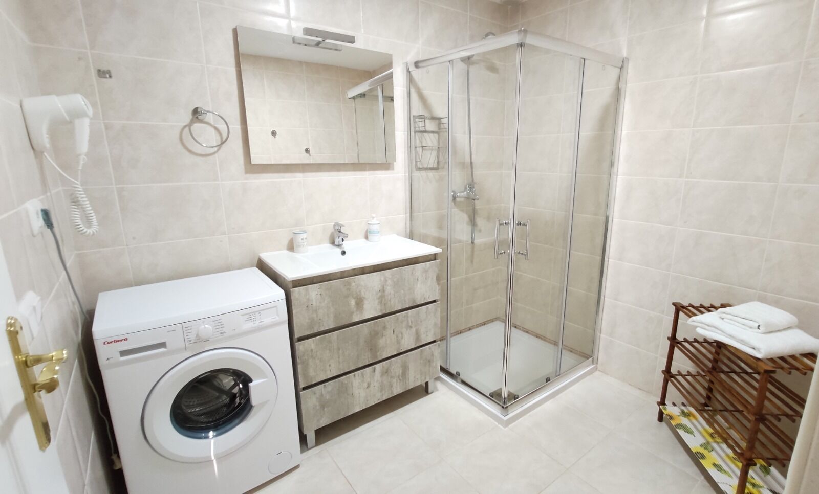 A modern bathroom with a washing machine, a glass-enclosed shower, a vanity with a mirror, and a towel rack.
