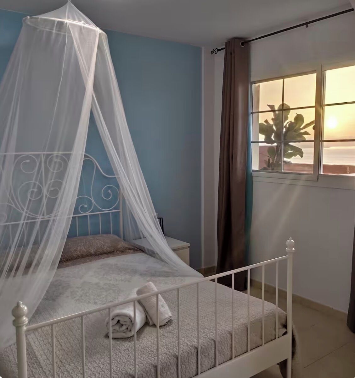 A bedroom with a bed, a window with curtains, and a view of the sea.