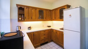 Une cuisine avec des meubles de rangement en bois, un réfrigérateur blanc et un plan de travail sur lequel se trouvent une bouilloire et un grille-pain.