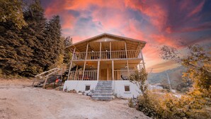 A two-story wooden cabin with a balcony, surrounded by trees and a dirt ground. - Abant İlbey Dağ Evi (Bolu)
