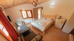 A cozy bedroom with a bed, a small table with a chair, a refrigerator, and a window with curtains. - Abant İlbey Dağ Evi (Bolu)