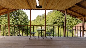 A covered outdoor area with a wooden deck, two tables, and chairs, overlooking a forested area. - Abant İlbey Dağ Evi (Bolu)