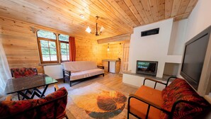 A cozy cabin interior with a wooden ceiling, a sofa, a dining table, and a fireplace. - Abant İlbey Dağ Evi (Bolu)