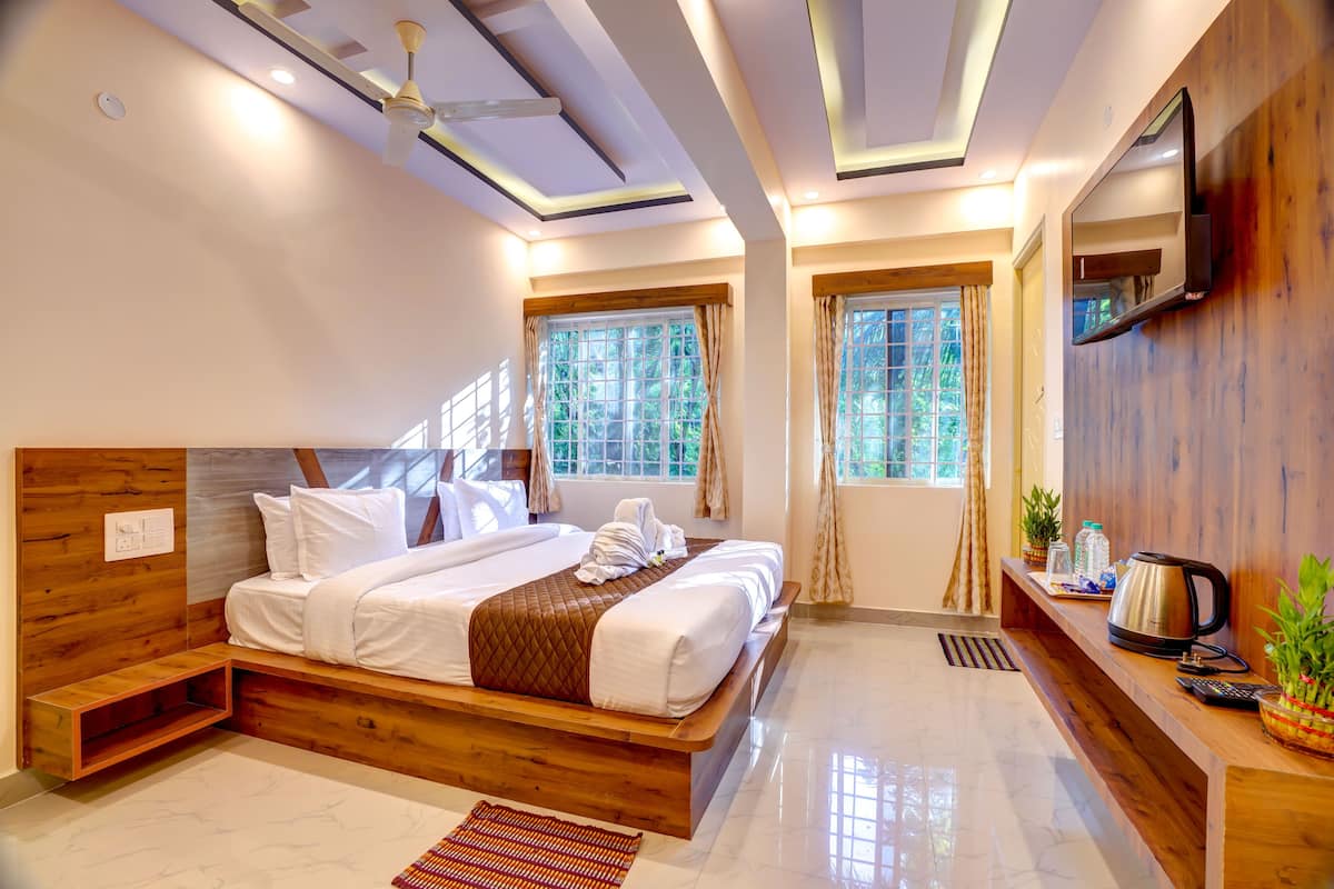 A modern bedroom with a wooden bed, a TV mounted on the wall, and a small kitchenette area.