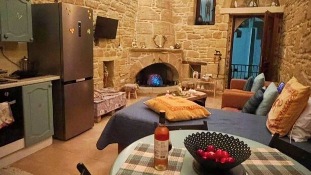 A cozy room with a stone wall, a fireplace, a dining table, and a sofa. - Rustic 2 Bedroom Stone Apartment in Malonas Rodos (Malonas Rodos)