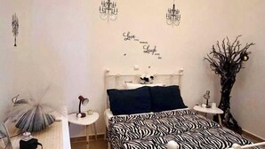 A bedroom with a zebra-patterned bed, a small bedside table, a lamp, a decorative wall piece, and a wall-mounted light fixture. - Rustic 2 Bedroom Stone Apartment in Malonas Rodos (Malonas Rodos)