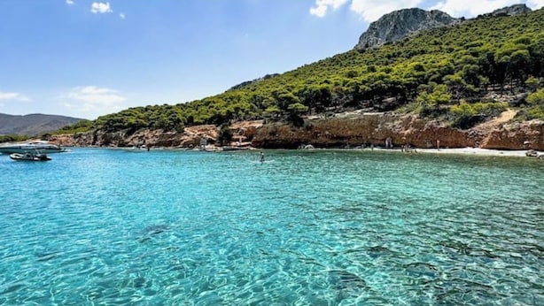 Un paysage côtier avec une eau turquoise et limpide, des bateaux et une chaîne de montagnes en arrière-plan.