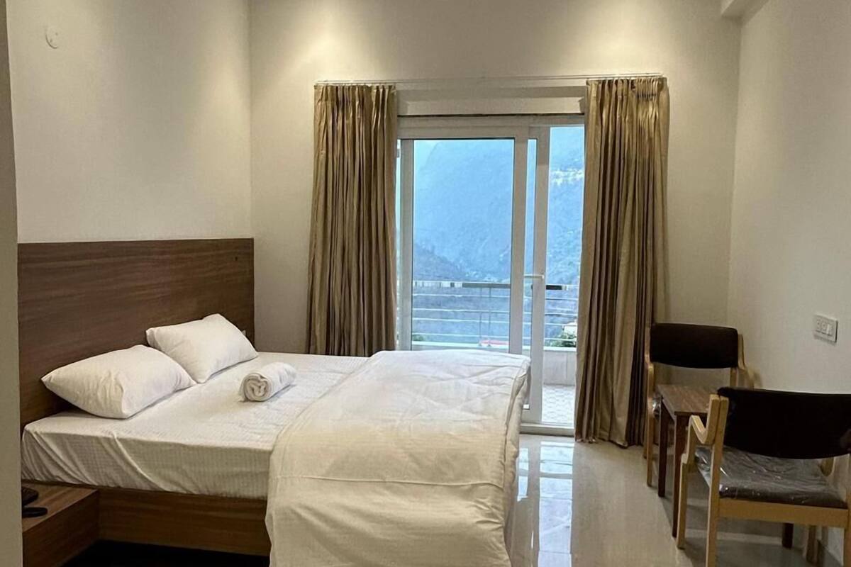 A hotel room with a bed, a desk, and a chair. There is a window with curtains, a ceiling fan, and a view of the outside.