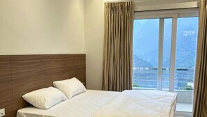 Habitación de hotel con una cama grande, un cabecero de madera, una mesita de noche con teléfono y vistas a las montañas desde la ventana.