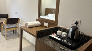 Habitación de hotel con escritorio de madera, espejo, cama, cafetera y bandeja con artículos de aseo.