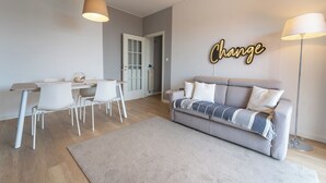 A modern living room with a sofa, a dining table with chairs, and a wall-mounted lamp. - Le Orchidee by Wonderful Italy (Sanremo)