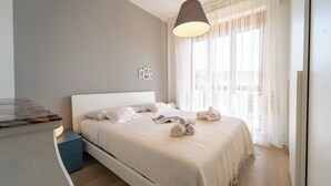 A neatly made bed with a white headboard, a hanging pendant light, and a view of a balcony through sheer curtains. - Le Orchidee by Wonderful Italy (Sanremo)