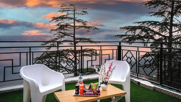 Un balcon avec deux chaises blanches, une petite table avec des collations et des boissons, et un vase de fleurs.