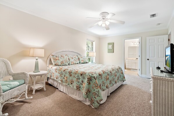 A bedroom with a bed, a rocking chair, a side table, a ceiling fan, and a television.