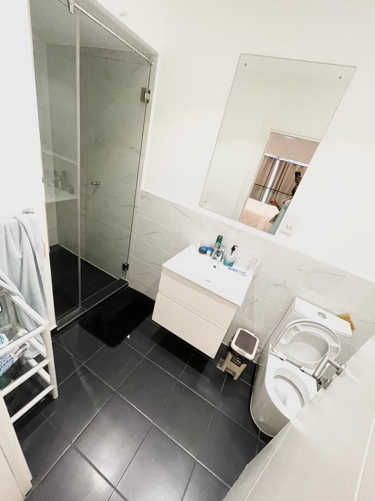 Et badeværelse med brusekabine i glas, en hvid vask med toiletartikler og et toilet.
