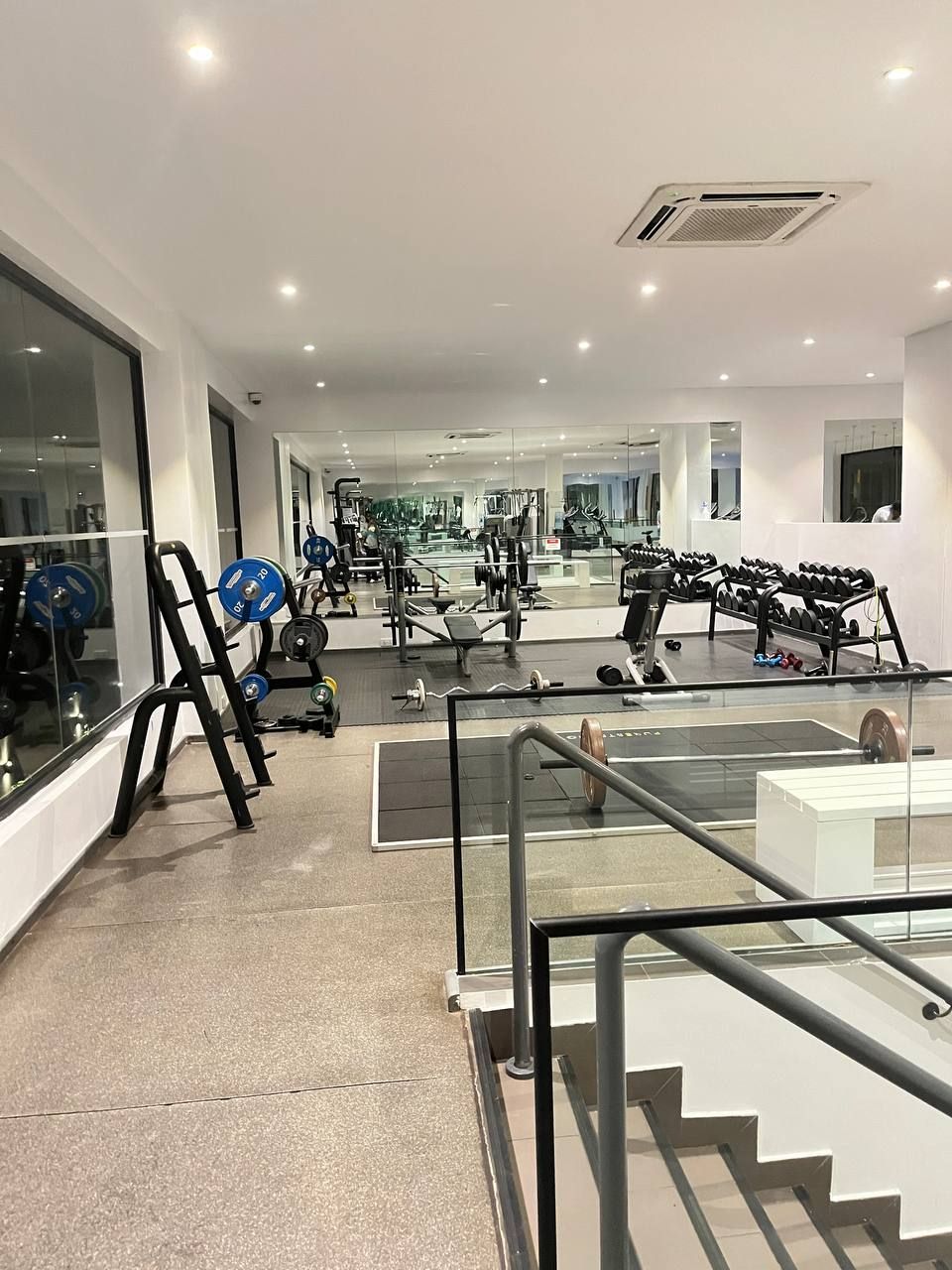 A modern gym with various exercise equipment, large mirrors, and a spacious layout.