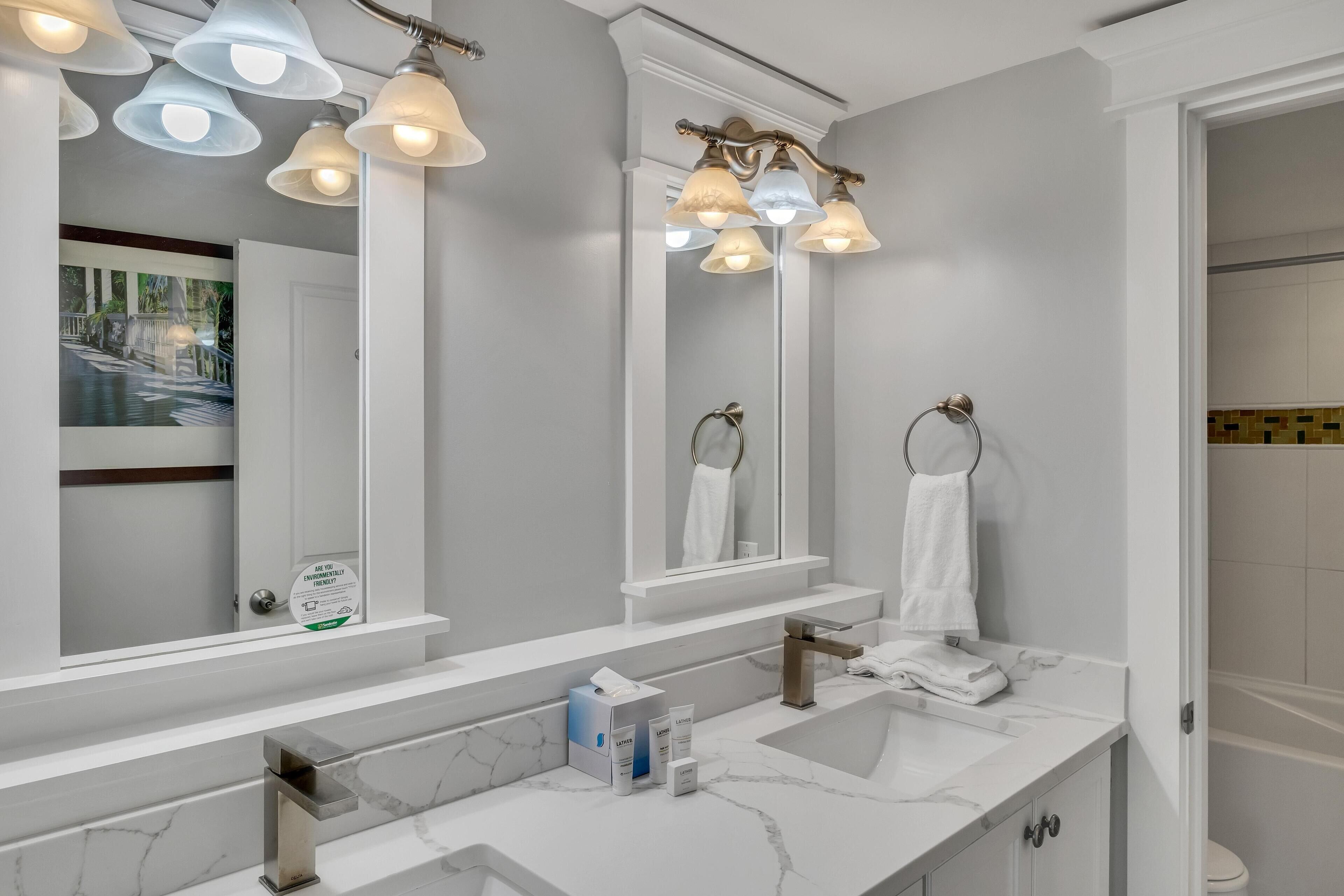 A modern bathroom with a large mirror, multiple light fixtures, a marble sink, and a towel rack.