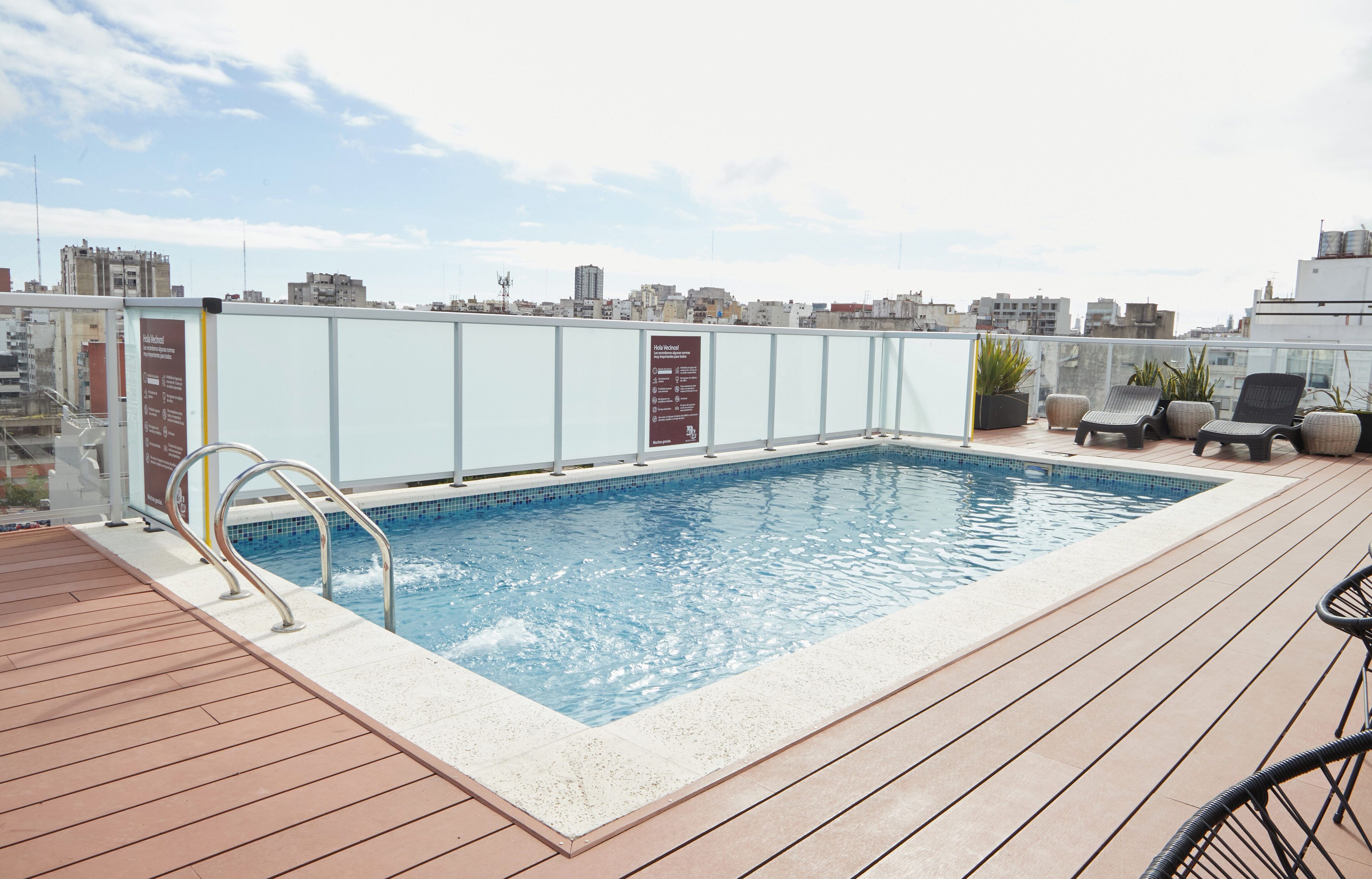 A rooftop pool with a wooden deck, lounge chairs, and a cityscape view.