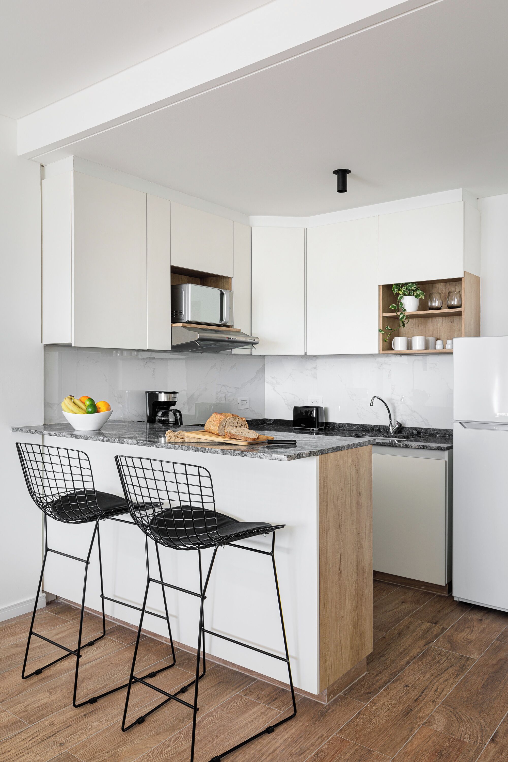 Una cocina moderna con armarios blancos, encimera de mármol, microondas integrado e isla de madera con taburetes de bar.