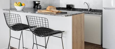 A modern kitchen with white cabinets, a marble countertop, a built-in microwave, and a wooden island with bar stools.