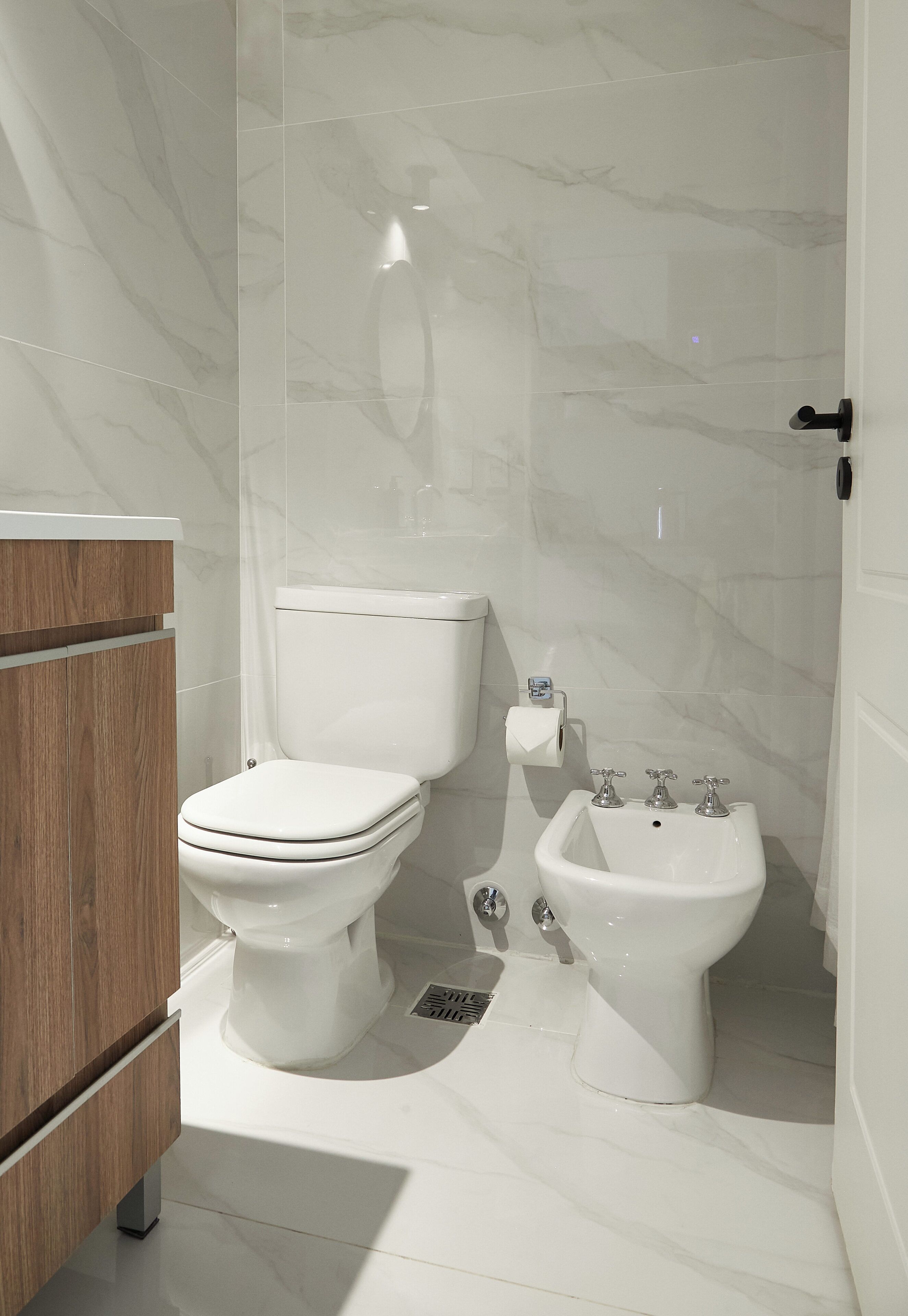 A modern bathroom with a toilet, bidet, and wooden vanity.