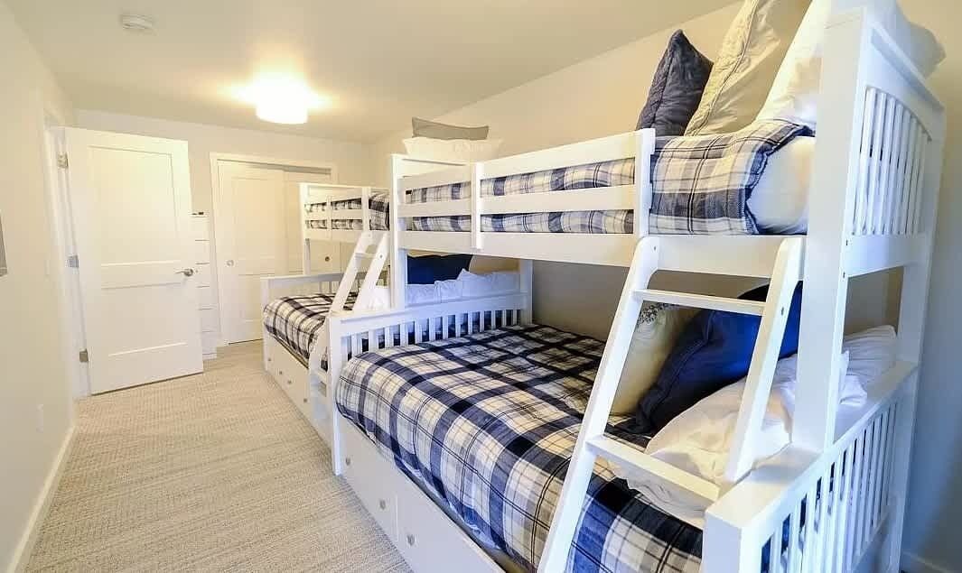 A bunk bed room with a plaid bedspread, white railings, and a door in the background.
