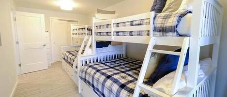 A bunk bed room with a plaid bedspread, white railings, and a door in the background.