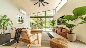 Ein modernes Wohnzimmer mit einer Couch, einem Sessel und großen Fenstern mit Blick auf Grünflächen.