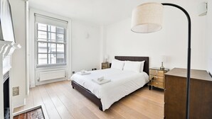 A bedroom with a large bed, bedside tables, a floor lamp, a window, and a radiator.