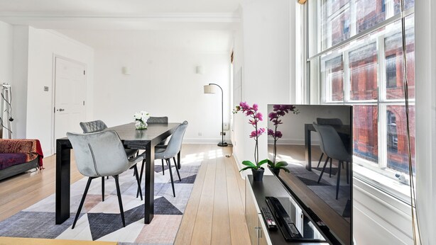 A modern living room with a dining area, a large window, and a view of a building.