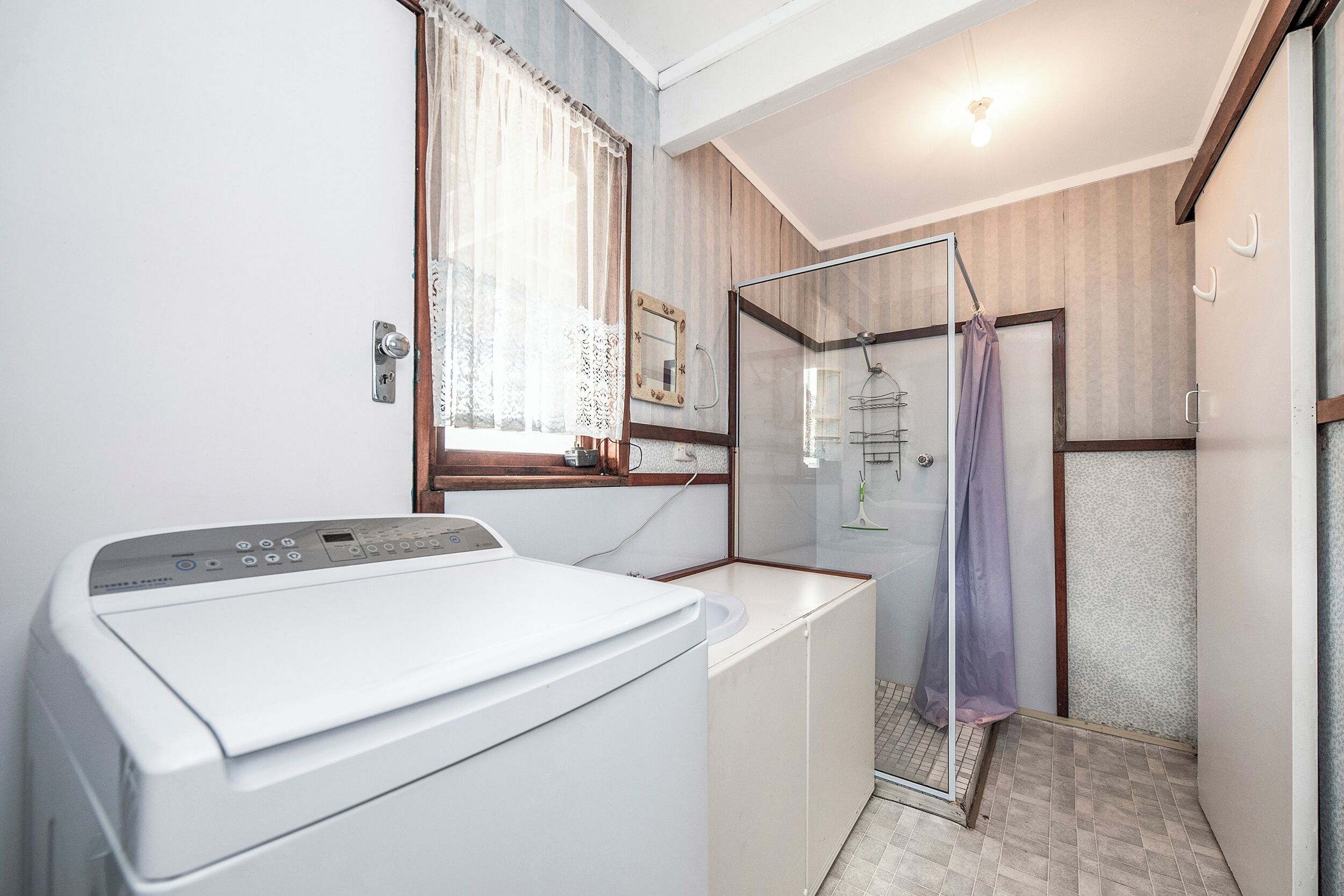 A compact bathroom with a washing machine, a glass shower enclosure, and a small sink.
