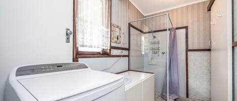 A compact bathroom with a washing machine, a glass shower enclosure, and a small sink.