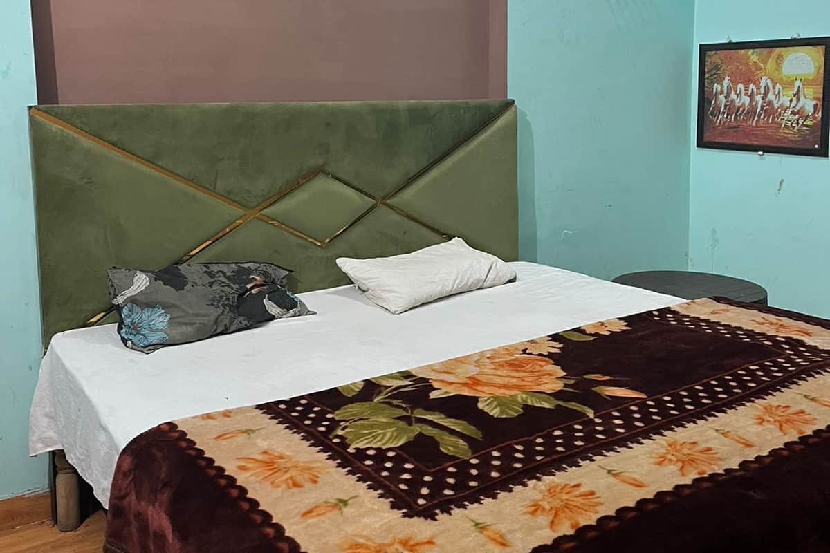 A bedroom with a bed, a green headboard, a floral bedspread, and a framed picture on the wall.