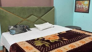 A bed with a green headboard, white bedding, and a floral-patterned bedspread. - Hotel Aryavart (Meerut)