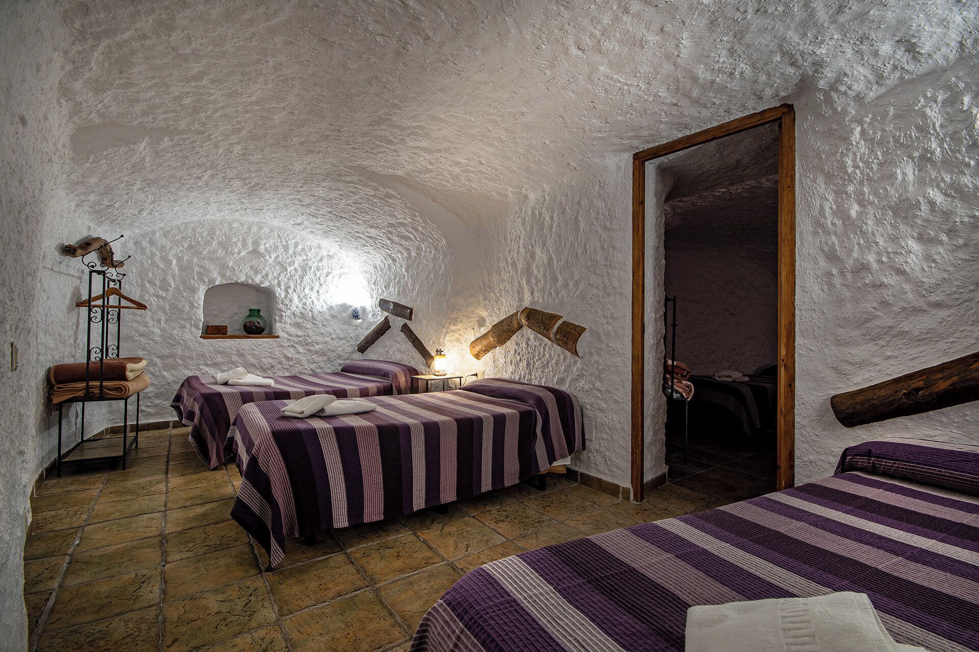A rustic room with three beds, a stone floor, and a white textured ceiling.